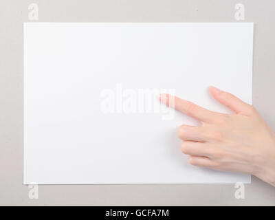 Woman`s finger pointing at the blank paper sheet. On gray cardboard background Stock Photo